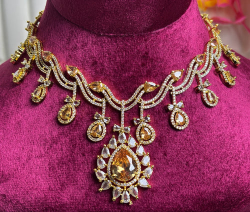 An ornate gold-toned statement necklace with clear stones and a large teardrop-shaped amber gemstone pendant, displayed on a magenta velvet jewelry bust.